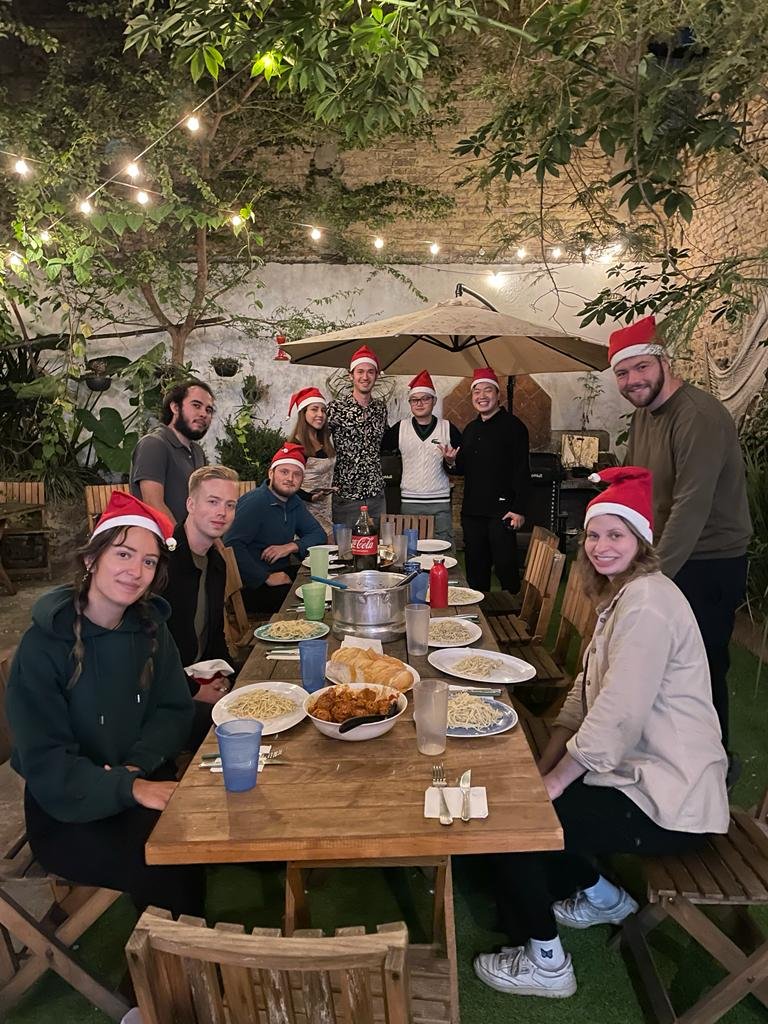 Grupo cenando con sombreros navideños al aire libre.