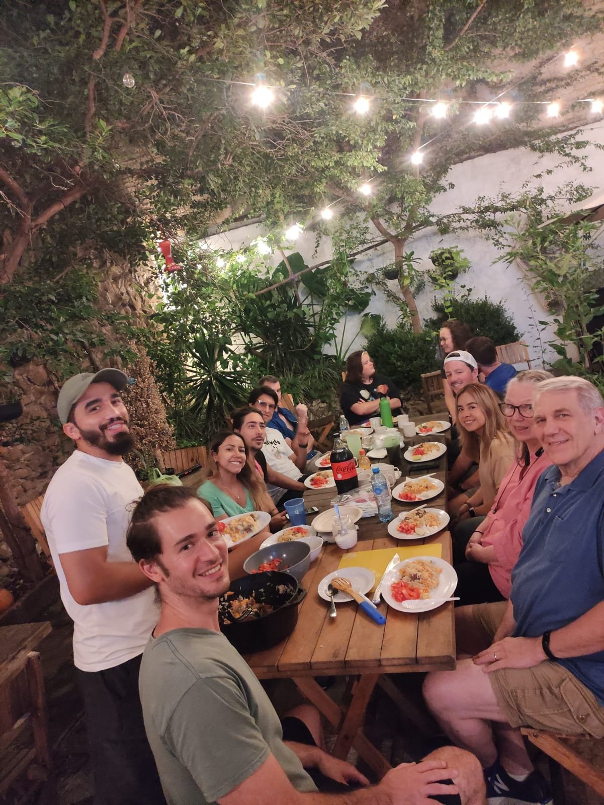 Personas cenando al aire libre en un jardín iluminado.