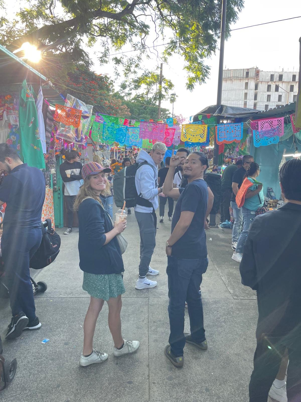 Personas paseando en mercado mexicano con papel picado colorido.
