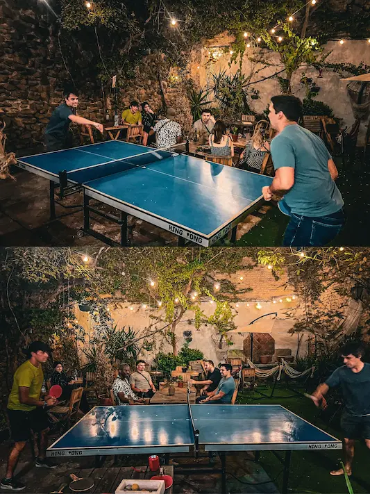 Personas jugando ping pong en un jardín iluminado.