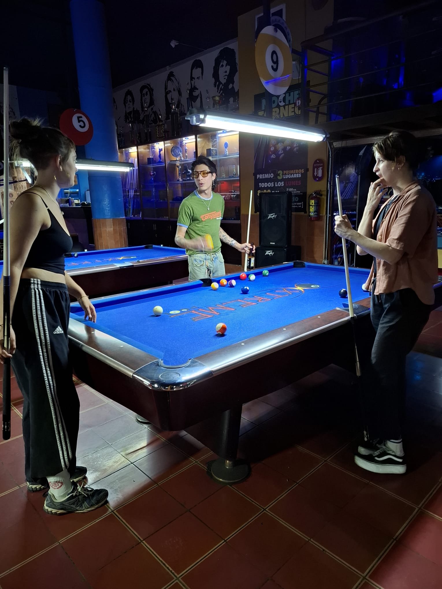Personas jugando billar en salón iluminado.