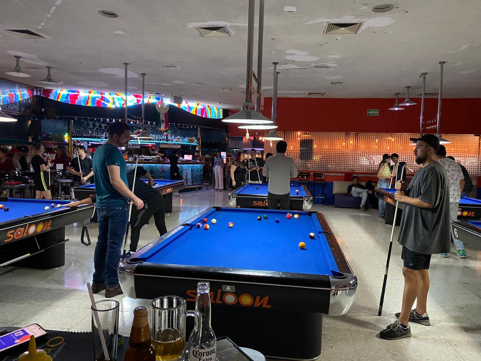 Personas jugando billar en un salón concurrido.