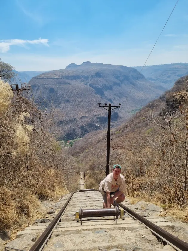 Persona en vías de tren, paisaje montañoso seco.