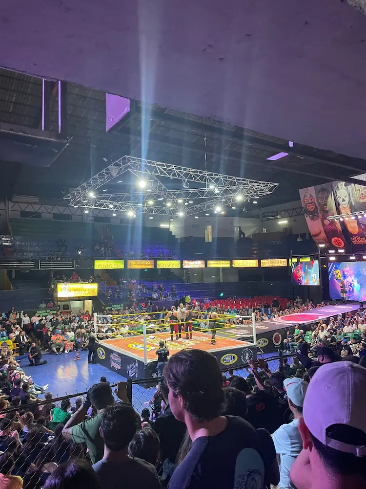 Lucha libre en arena con público entusiasta.
